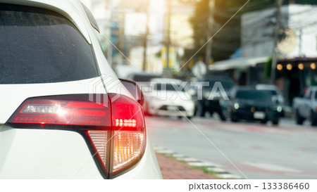 Rear side of white car with turn on brake light. Cars on the opposite side are lined up waiting for the traffic light at the intersection. Blurred of town at day. 133386460