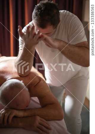 Professional therapist applying deep tissue massage techniques on a male client lying on massage table with towel, therapeutic bodywork for muscle pain relief and relaxation. Professional therapist applying deep tissue massage techniques on a male client lying on massage table with towel, therapeutic bodywork for muscle pain relief and relaxation. 133386563
