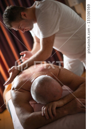 Professional therapist applying deep tissue massage techniques on a male client lying on massage table with towel, therapeutic bodywork for muscle pain relief and relaxation. Professional therapist applying deep tissue massage techniques on a male client lying on massage table with towel, therapeutic bodywork for muscle pain relief and relaxation. 133386569