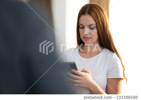 Two young women in casual white shirts smiling and looking at a smartphone screen together indoors. Concept of friendship, social connection, communication, and modern lifestyle. Two young women in casual white shirts smiling and looking at a smartphone screen together indoors. Concept of friendship, social connection, communication, and modern lifestyle. 133386580