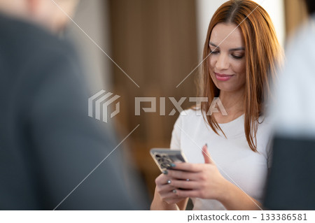 Two young women in casual white shirts smiling and looking at a smartphone screen together indoors. Concept of friendship, social connection, communication, and modern lifestyle. Two young women in casual white shirts smiling and looking at a smartphone screen together indoors. Concept of friendship, social connection, communication, and modern lifestyle. 133386581