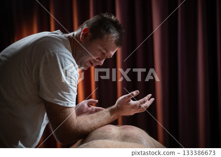Professional male massage therapist performing deep tissue back massage on an older man lying on a massage table covered with a towel. Relaxing wellness treatment in a modern spa room with warm light Professional male massage therapist performing deep tissue back massage on an older man lying on a massage table covered with a towel. Relaxing wellness treatment in a modern spa room with warm light 133386673