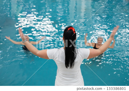 Instructor leading aquatic fitness training for group senior women in a swimming pool. Concept of health, exercise, wellness, water therapy, and active aging lifestyle 133386801
