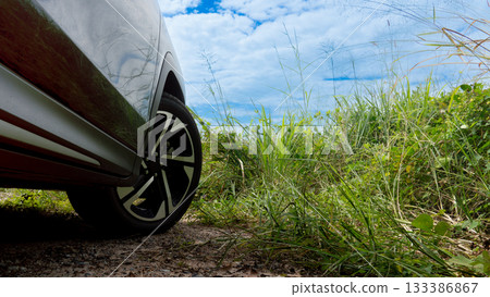 Under view of dark car Driving on a dirt road. Front wheels spin out when the car stops or makes a U-turn. Found grass covering the entire area. Under blue sky and white clouds. 133386867
