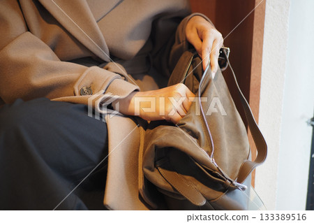 Woman reaching into a stylish bag at a cozy location Woman reaching into a stylish bag at a cozy location 133389516