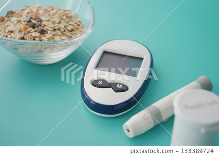 Glucose monitor next to bowl of oatmeal on turquoise table Glucose monitor next to bowl of oatmeal on turquoise table 133389724
