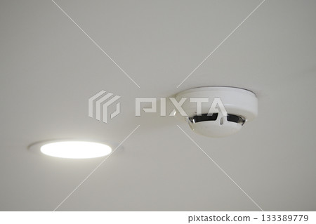Smoke detector installed on ceiling with ceiling light 133389779