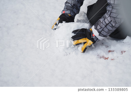 Child plays in snow making a snowball in winter 133389805