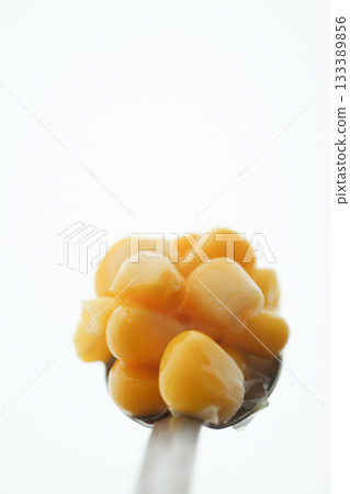 Close-up of sweet corn on a spoon against a white background 133389856