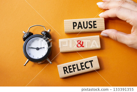Pause and Reflect symbol. Concept words Pause and Reflect on wooden blocks. Businessman hand. Beautiful orange background with alarm clock. Business and Pause and Reflect concept. Copy space. 133391355