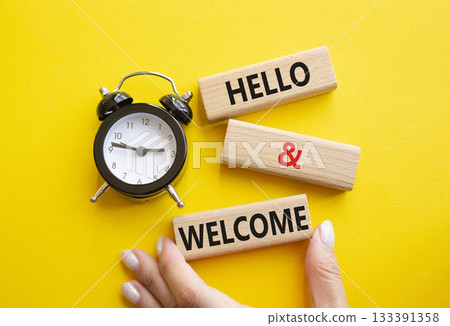 Hello and Welcome symbol. Concept words Hello and Welcome on wooden blocks. Businessman hand. Beautiful yellow background with alarm clock. Business and Hello and Welcome concept. Copy space. Hello and Welcome symbol. Concept words Hello and Welcome on wooden blocks. Businessman hand. Beautiful yellow background with alarm clock. Business and Hello and Welcome concept. Copy space. 133391358