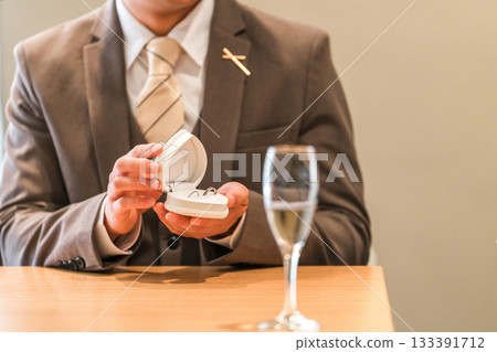 A man in a suit and tuxedo opening a jewelry case and ring case to show off a ring (marriage proposal) 133391712