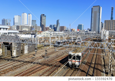 一列關西線313系普通列車行駛在路上，背景是名古屋站的摩天大樓。 133392470