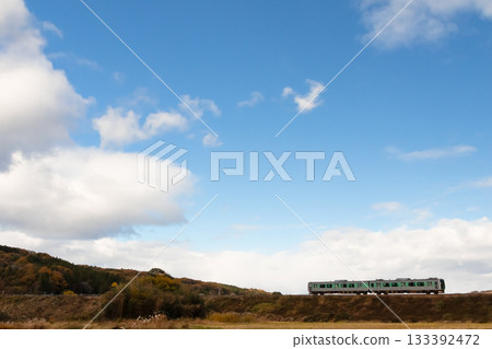 一列本地火車在晴朗的藍天和雲下行駛。 133392472