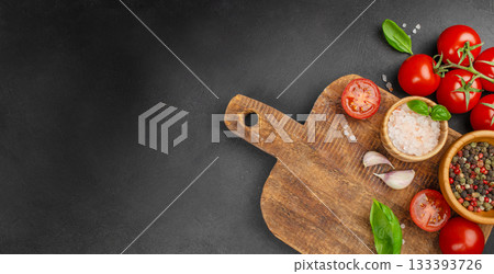 Rustic wooden cutting board with fresh tomatoes, basil, garlic and spices arranged on dark stone background, top view with wide copy space for recipe text, menu design or cooking concepts Rustic wooden cutting board with fresh tomatoes, basil, garlic and spices arranged on dark stone background, top view with wide copy space for recipe text, menu design or cooking concepts 133393726