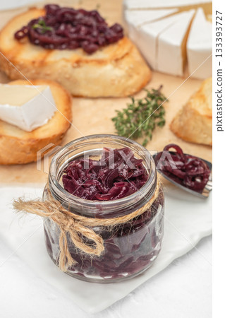 Homemade caramelized red onion jam in a glass jar with rustic twine, served alongside toasted bread, brie cheese and fresh thyme 133393727