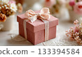 Delicate pink gift box adorned with ribbon surrounded by seasonal flowers on a textured table 133394584