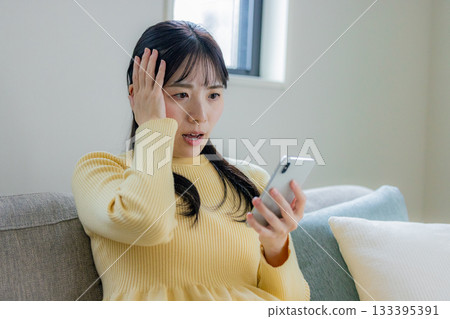 A woman sitting on the sofa and using a smartphone 133395391