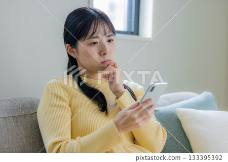 A woman sitting on the sofa and using a smartphone 133395392
