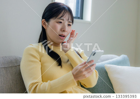 一個女人坐在沙發上使用智能手機 133395393