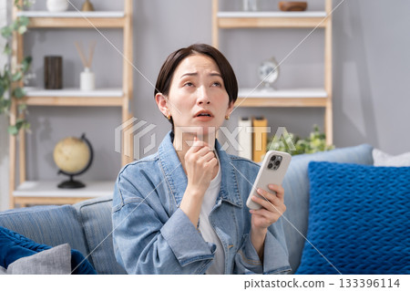 客廳裡一位拿著智慧型手機的女士感到擔憂。 133396114