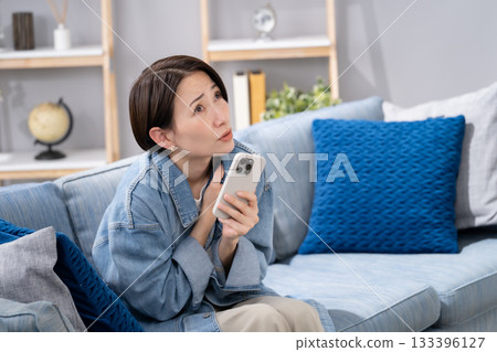 A woman holding a smartphone in the living room. It's cold. A woman holding a smartphone in the living room. It's cold. 133396127