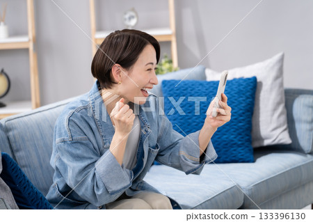 Woman holding a smartphone in the living room Woman holding a smartphone in the living room 133396130