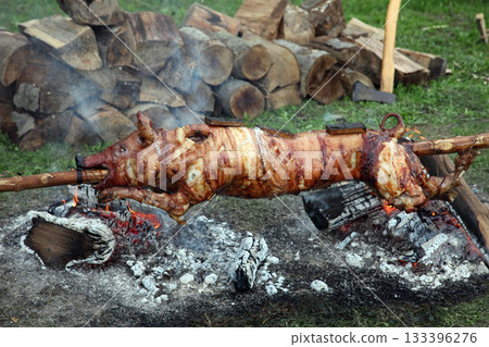 Suckling pig on a rotating spit with fire in the background 133396276