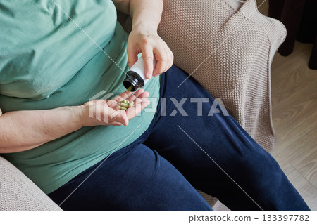 Mature woman pouring green capsules from bottle into her hand for daily health 133397782