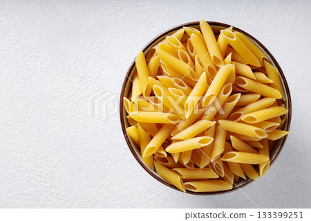 Uncooked Penne Pasta in Ceramic Bowl on White Textured Background Uncooked Penne Pasta in Ceramic Bowl on White Textured Background 133399251