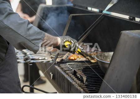 Male chef preparing meat on grill at barbecue party in summer garden Male chef preparing meat on grill at barbecue party in summer garden 133400138