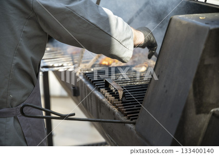 Male chef preparing meat on grill at barbecue party in summer garden Male chef preparing meat on grill at barbecue party in summer garden 133400140