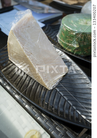 a piece of cheese in clear packaging at a farmers market. a piece of cheese in clear packaging at a farmers market. 133400207