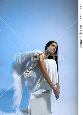 Studio photo of sexy blonde in white long dress and angel wings, she poses on blue background 133400568