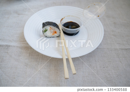 sushi roll with chopsticks and wasabi sauce in a plastic container on a white plate. 133400588