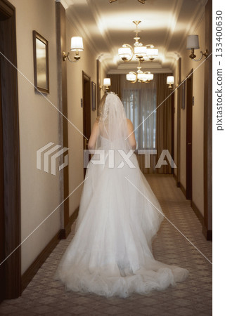 beautiful blonde bride with veil in hotel hallway in fashionable dress, back view. beautiful blonde bride with veil in hotel hallway in fashionable dress, back view. 133400630