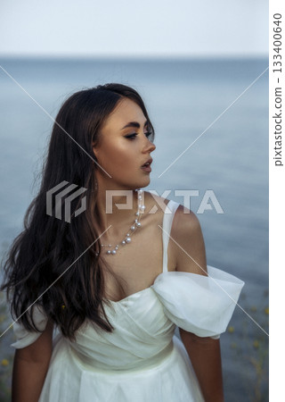 portrait of a beautiful young woman with bright make-up and in a long white dress. 133400640