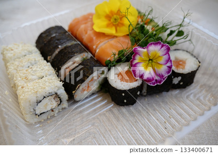 Mix of sushi rolls with salmon, avocado, smoked eel, in a plastic food delivery box. 133400671