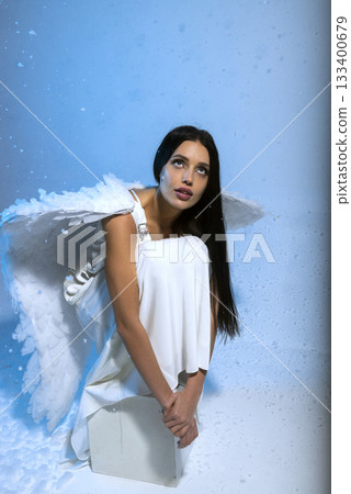 studio photo of blonde in white long dress and angel wings posing on blue background in studio 133400679