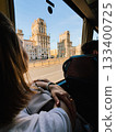 Young woman admiring the stunning Gates of Minsk from window of tourist bus, soaking in vibrant cityscape on bright, sunny day filled with exploration and adventure. Traveler gazing through bus window 133400725