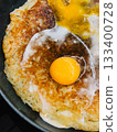 Close up of crispy potato pancake topped with fried egg cooking in frying pan, creating visually appealing and delicious breakfast dish. Crispy potato pancake with sunny side up egg in iron skillet 133400728