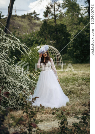 Elegant Bride in a Flowing White Gown Surrounded by Lush Greenery Elegant Bride in a Flowing White Gown Surrounded by Lush Greenery 133400748