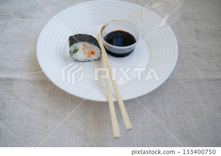 sushi roll with chopsticks and wasabi sauce in a plastic container on a white plate sushi roll with chopsticks and wasabi sauce in a plastic container on a white plate 133400750