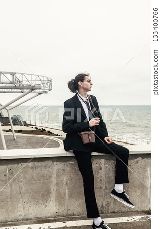 A young man sits alone against the backdrop of modern architecture near the sea. A young man sits alone against the backdrop of modern architecture near the sea. 133400766