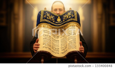 A Jewish man holds an open Torah scroll during a sacred ceremony. The glowing light highlights the spiritual moment, perfect for themes of faith, tradition, and Jewish holidays. 133400848