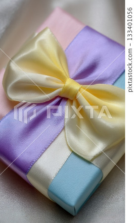 A close-up of a gift box wrapped in pastel satin ribbons with a yellow bow. This gentle and festive image evokes joy and surprise. Perfect for greeting cards or holiday designs. 133401056