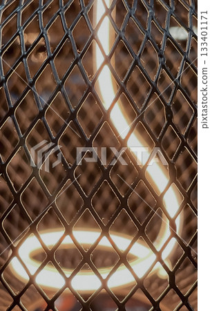 Close-up of a warm glowing LED filament light bulb inside a diamond metal mesh cage Close-up of a warm glowing LED filament light bulb inside a diamond metal mesh cage 133401171