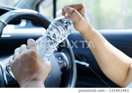 Asian woman driver holding water bottle in car. 133401463