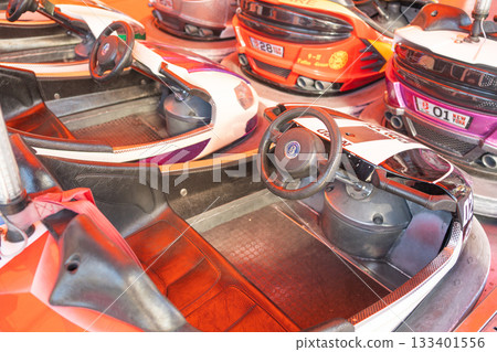 A group of bumper cars stands ready inside the amusement arena. Bright lights illuminate the vibrant vehicles, emphasizing the classic fairground atmosphere A group of bumper cars stands ready inside the amusement arena. Bright lights illuminate the vibrant vehicles, emphasizing the classic fairground atmosphere 133401556