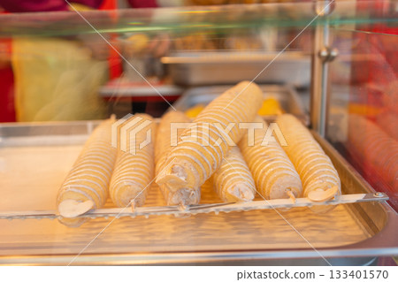 Raw spiral-cut potatoes coated in batter and arranged on sticks before deep-frying. The close-up highlights their textured surface and uniform shape, capturing a classic street-food preparation moment Raw spiral-cut potatoes coated in batter and arranged on sticks before deep-frying. The close-up highlights their textured surface and uniform shape, capturing a classic street-food preparation moment 133401570